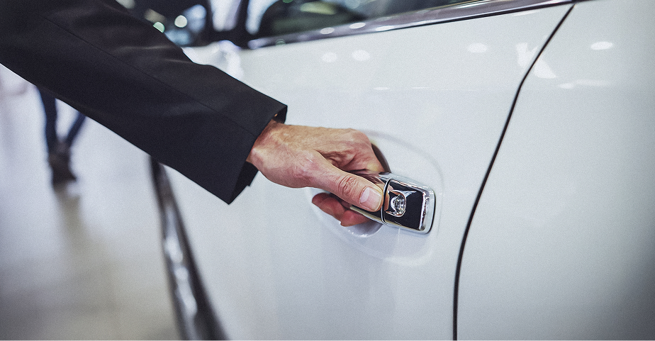 Primer plano de la mano de una persona abriendo la manija cromada de la puerta de un auto blanco.